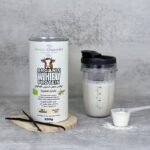 Shaker containing whey protein shake next to a can of organic whey protein powder with vanilla